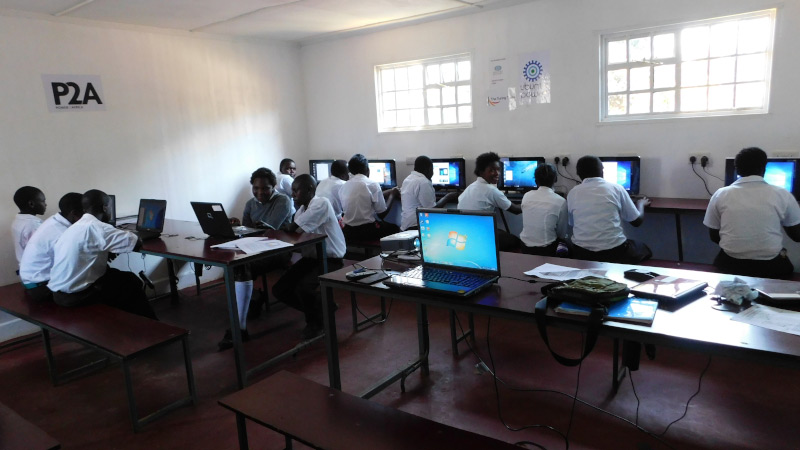 A bright sunny African classroom with uniformed students using laptops and computers